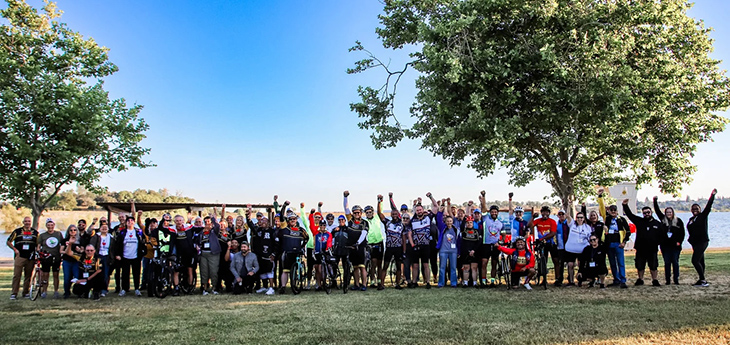 Group of people stand in line, shoulder to shoulder, many with bicycles.
