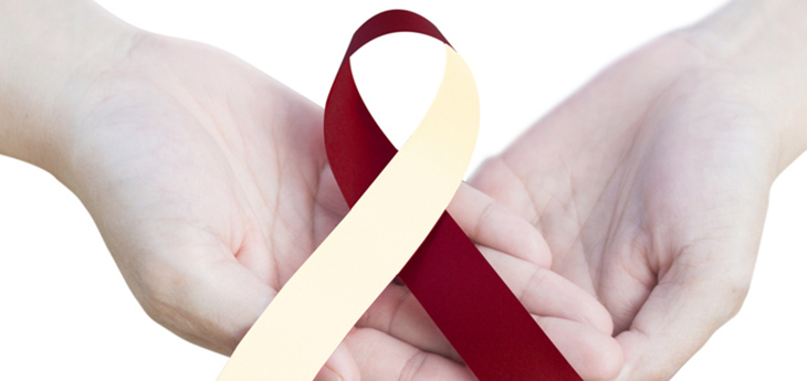 Head and neck cancer awareness ribbon (burgundy and ivory) held in hand on white background