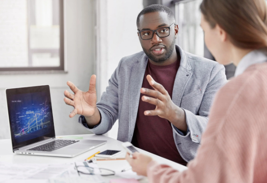 employees sitting together at a desk with a laptop in conversation