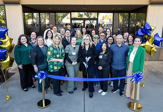 Group of staff and providers gather with scissors to cut blue ribbon