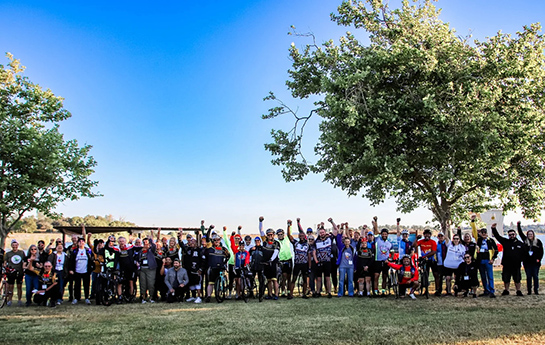 Group of people stand in line, shoulder to shoulder, many with bicycles.