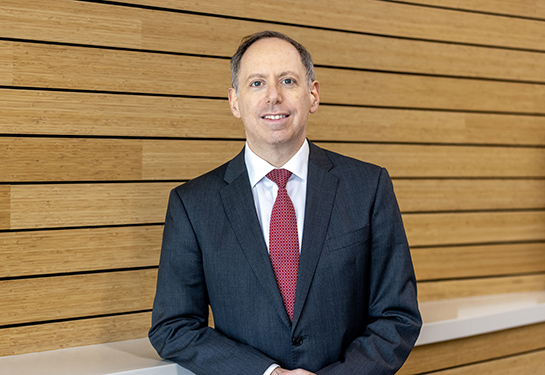 A man in a gray suit and red tie poses for a portrait indoors. 