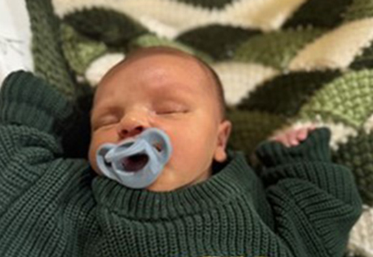 Sleeping baby boy wearing a green sweater with his name Ayden Sadegh JP Izquierdo on it.