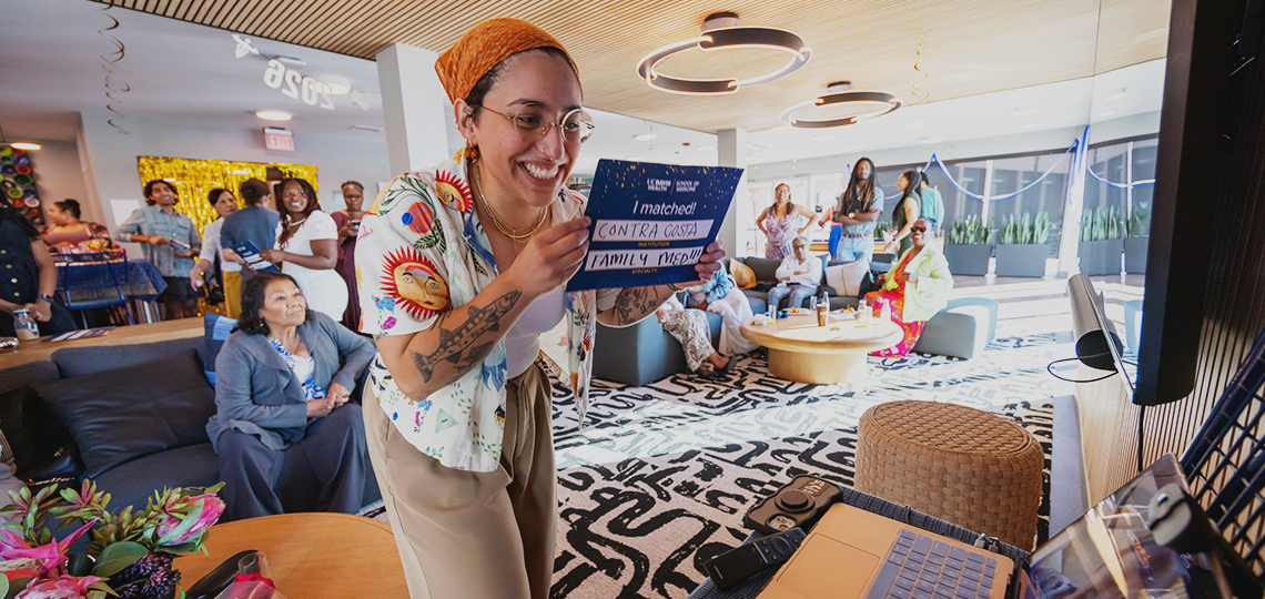 A medical student holds an “I Matched: Contra Costa Family Medicine” placard for her classmates to see in a video meeting.