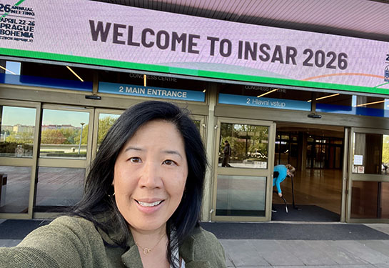 Christine Wu Nordahl poses for a selfie in front of a conference center in Prague. A sign above the center says Welcome to INSAR 2026