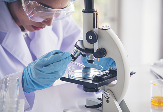 Scientist in PPE uses a pipette to add a drop of blood under a microscope