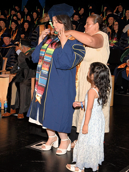 Medical school graduate Yakelin Arroyo Velazquez is hooded by her mother Anita as daughter Violet watches.