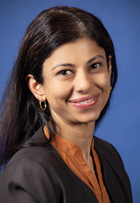 Woman with long dark hair, wearing blue jacket and maroon shirt, smiling into camera.