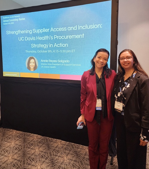 Two attendees stand in front of a presentation screen titled “Strengthening Supplier Access and Inclusion: UC Davis Health’s Procurement Strategy