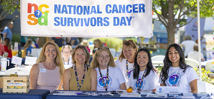 Six women sit under a sign that reads National Cancer Survivors Day