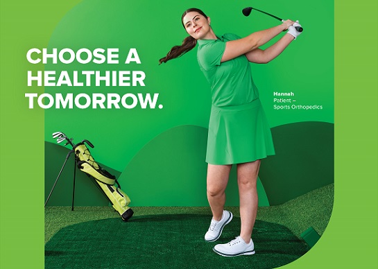 A person in green golf attire swings a golf club on a stylized green course with golf bag nearby.