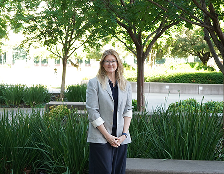 A person stands outside in front of trees and greenery
