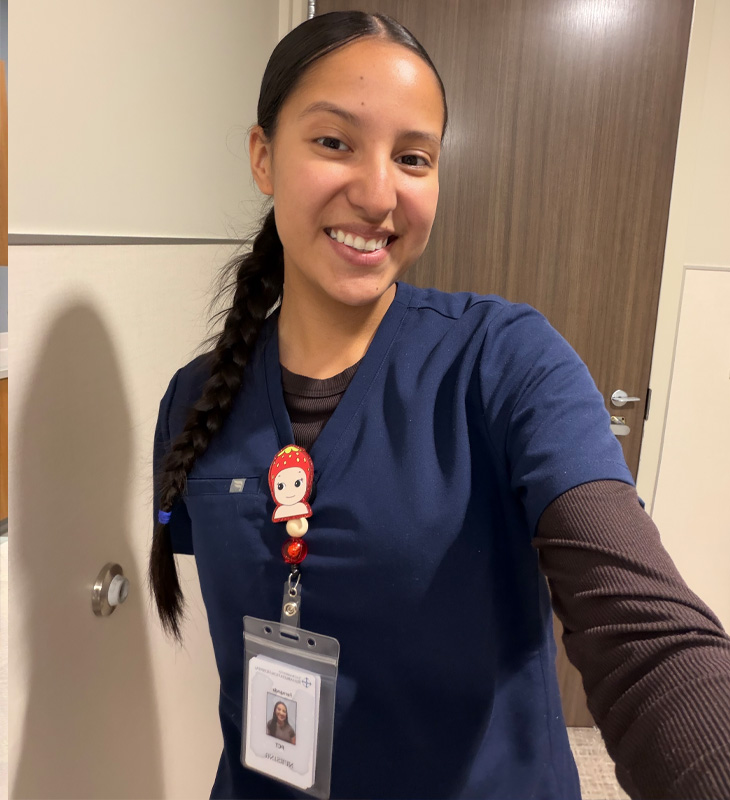 Nursing assistant smiles while wearing scrubs and a name badge.