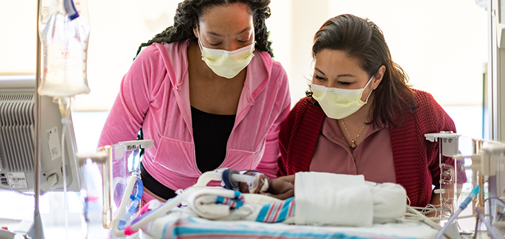 Two people stand over a NICU baby in a hospital