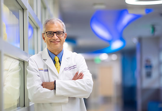 Man in white coat folds arms and smiles at camera