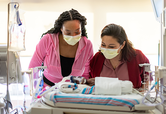Two people stand over a NICU baby in a hospital