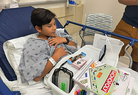 Child in gown laying in a hospital bed playing a game.