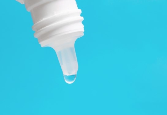 Close-up of an eye drop bottle tip with a single droplet against a blue background.