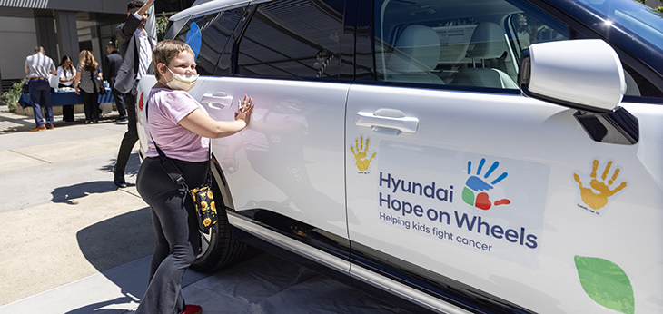 A child wearing a mask puts her painted hands on the white Hyundai SUV. 