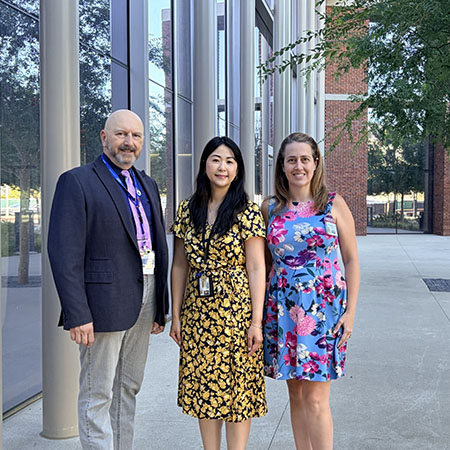 Three adults stand outside a steel and glass building at UC Davis Health