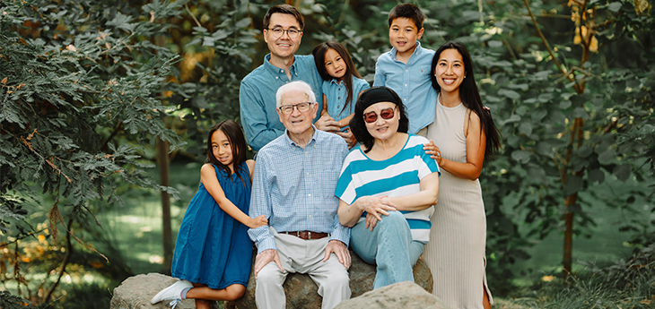 Multi-generational family portrait with seven people, including Charlotte Zhang, among trees and large rocks in a garden setting