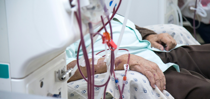 Patient undergoing dialysis is seated beside medical equipment in a healthcare facility.