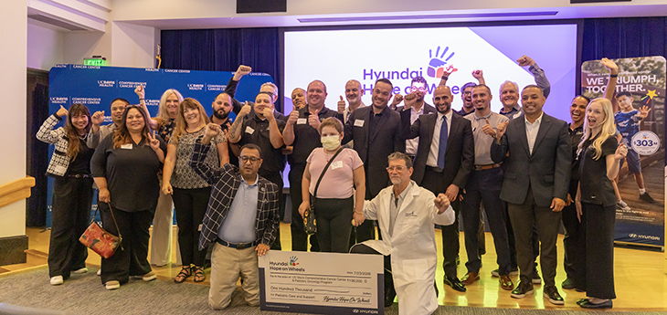 Twenty-three people gather on stage, surrounding a $100,000 enlarged check from Hyundai Hope on Wheels.