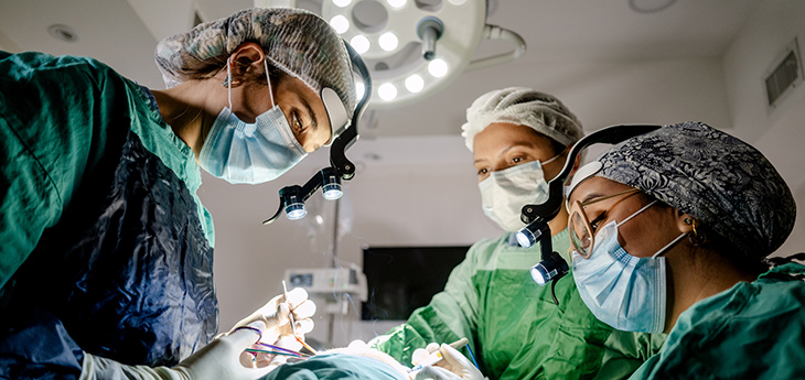 3 cirujanos trabajan en una sala de operaciones oscurecida.