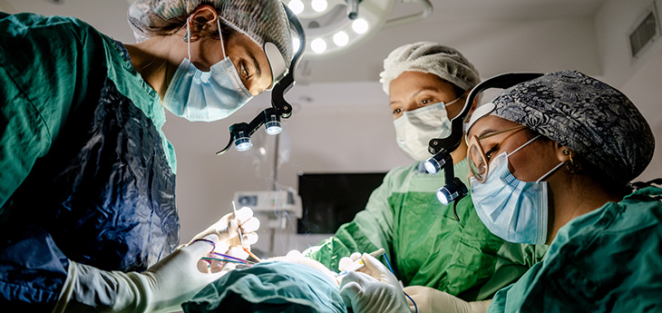 Three individuals on a surgical team work in an operating room.