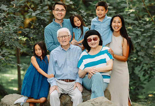 Multi-generational family portrait with seven people, including Charlotte Zhang, among trees and large rocks in a garden setting