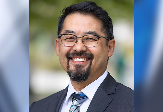 Portrait of Hendry Ton wearing glasses, a suit jacket and a patterned tie outdoors.