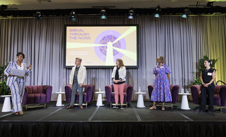 Panelists participate in a discussion on stage with a "Signal Through the Noise" presentation displayed behind them.