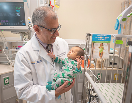 A person in a white coat holds baby in the hospital.