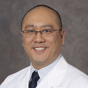 Physician Edward Kim, wearing a white physician’s coat, smiling.