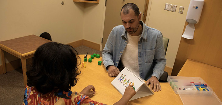 A health care provider sits across from a child at a table doing a behavioral health assessment