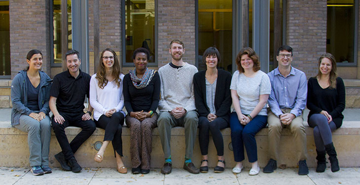 A group of nine adults sits on a cement bench outside the UC Davis MIND Institute 
