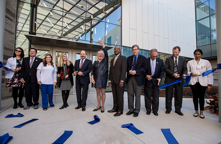 Group of leaders and students celebrate after cutting a blue ribbon outside Betty Irene Moore Hall