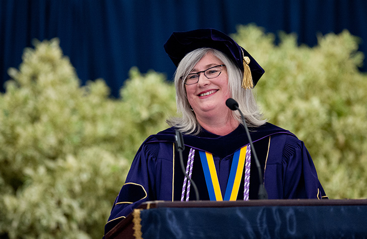 Heather Young smiles at a podium while wearing academic regalia during a School of Nursing ceremony.