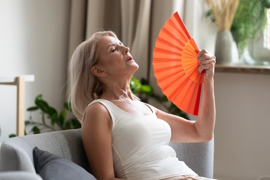 Woman wearing a tank top using a handheld fan to cool herself down