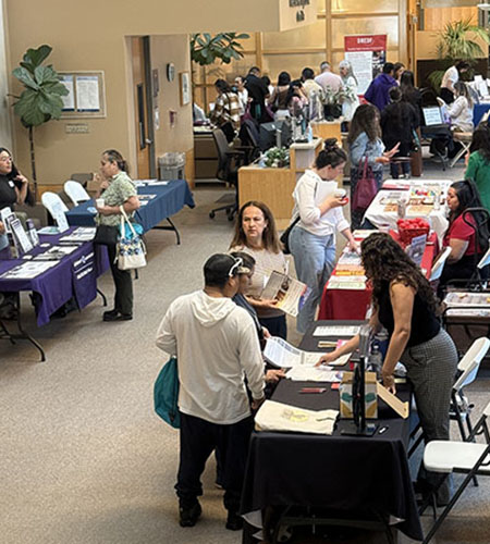 Adult conference attendees gather around information tables in the MIND Institute lobby. 