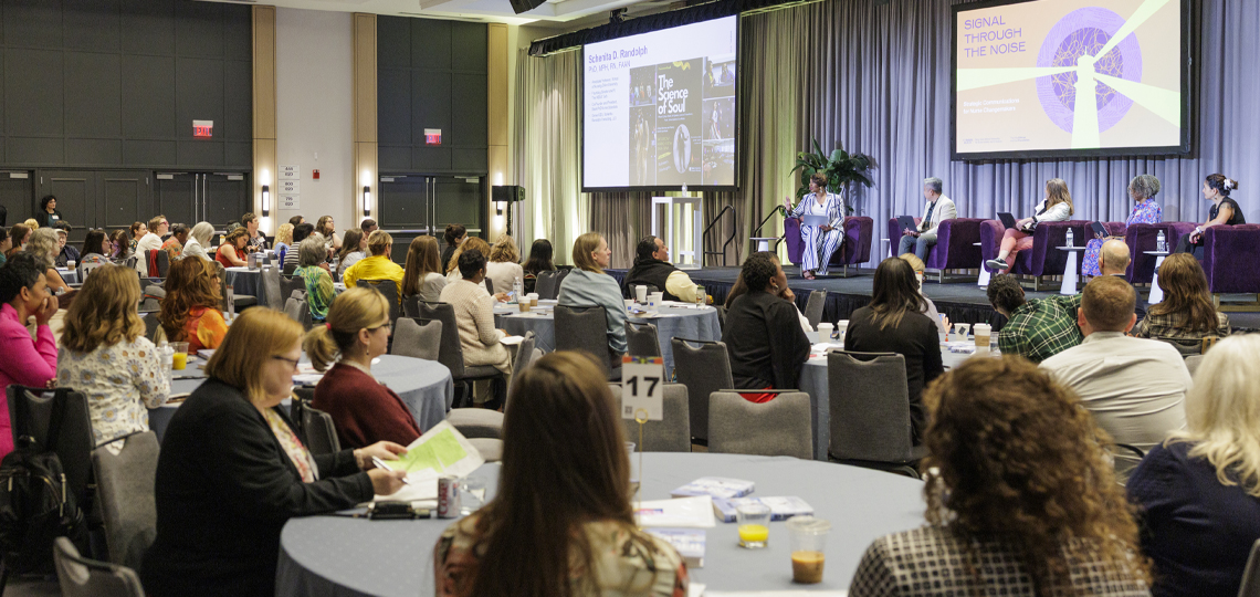Audience members watch a panel discussion with speakers seated onstage for a “Signal Through the Noise” session.