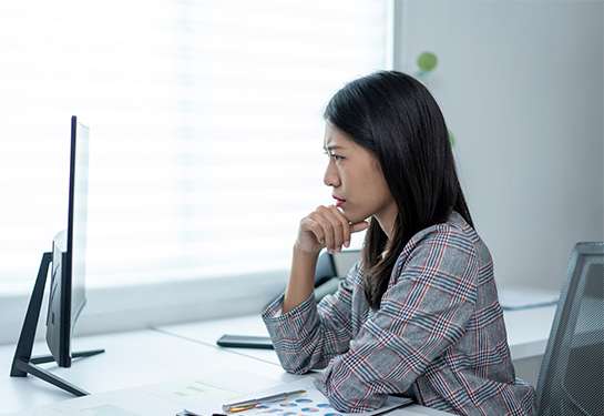Woman in plaid jacket, resting elbow on desk with concerned look on her face while viewing computer screen.