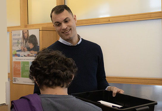 A smiling man holds a large black box while talking to a patient in a medical clinic