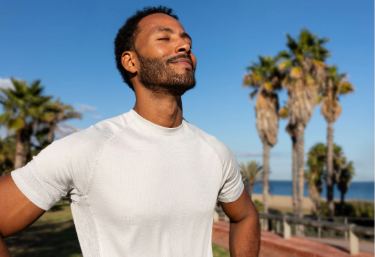 Man breathing deeply with palm trees and ocean in background.