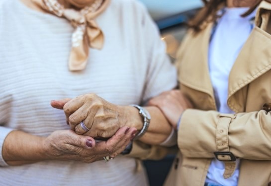 Close-up of one person holding an older adult’s hand while walking arm in arm.