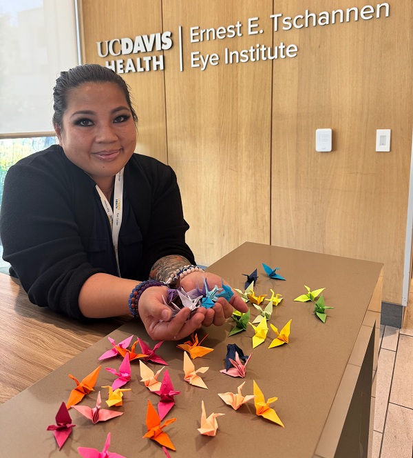 Staff member holds several colorful origami cranes while dozens of folded paper cranes are displayed on the reception desk at the Ernest E. Tschannen Eye Institute as part of a community art project.