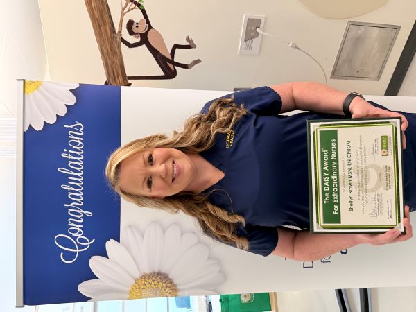 Shellyn stands with DAISY Award in front of banner. 