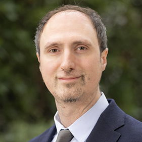 A man in a light blue suit and tie smiles.