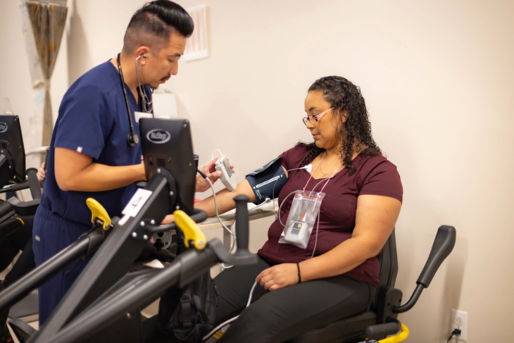A clinician checks a patient's blood pressure and monitoring equipment during a cardiac rehabilitation appointment.