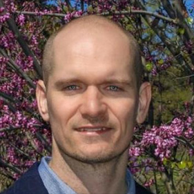 Portrait of David E. Olson outdoors, wearing a blue blazer and button-down shirt.
